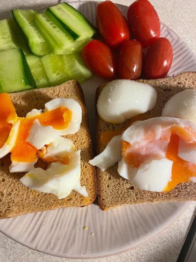 Två skivor brunt bröd med ägg, skivor av gurka och körsbärstomater.